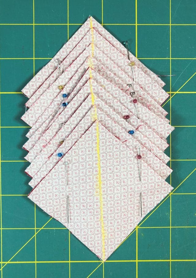 Squares of fabric are pinned in pairs, right sides facing, with a marked line corner to corner and pins on either side of the line.
